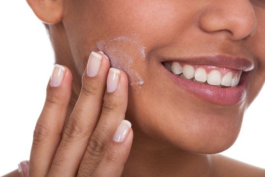 Smiling woman applying cosmetic cream to her cheek.