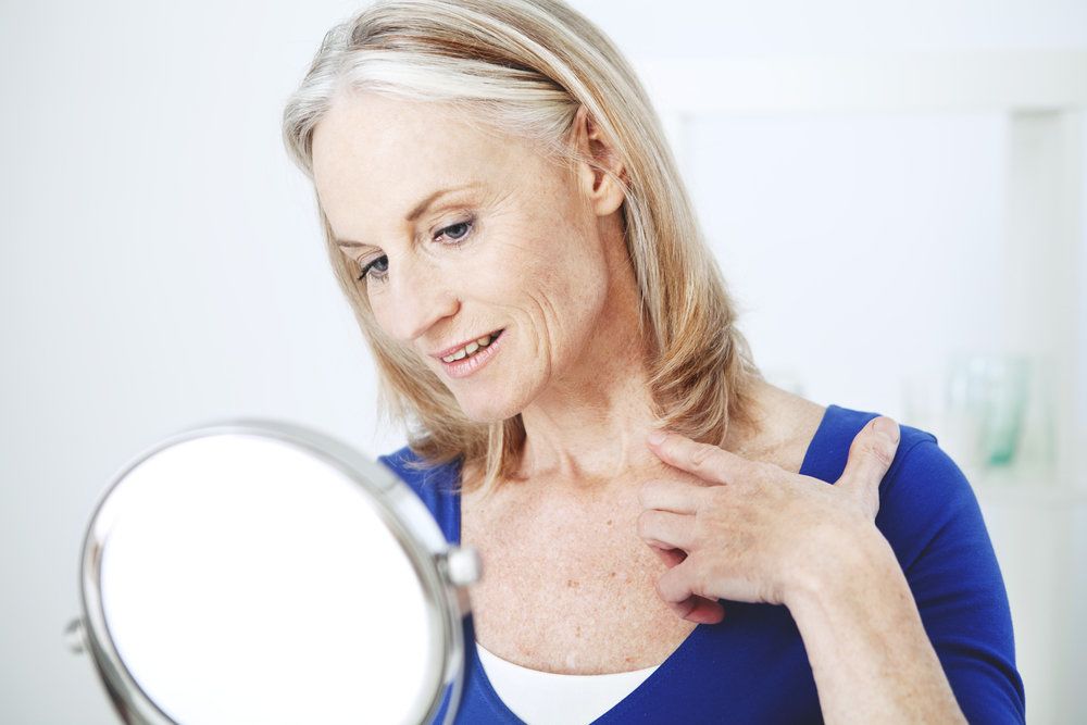 Older woman looking at her neck in a mirror.